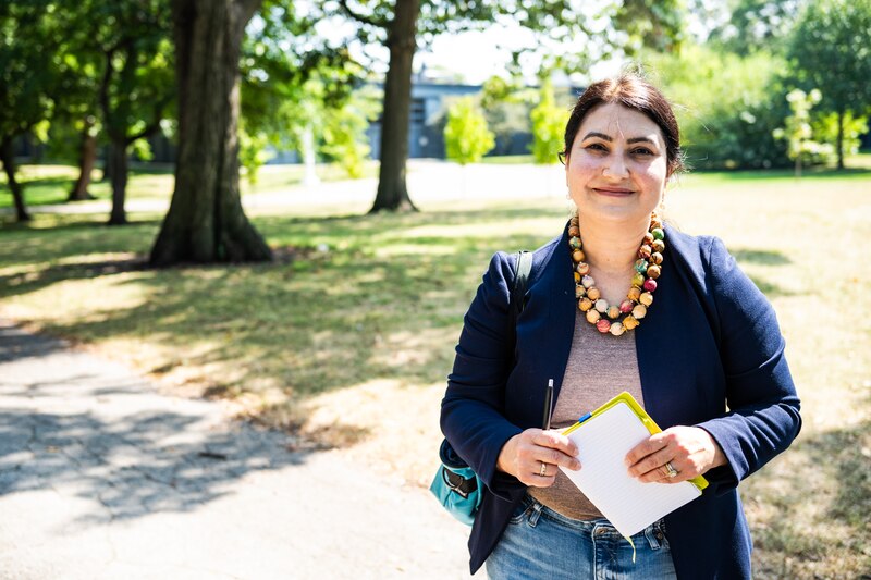 A woman wearing a dark suit jacket and holding papers poses for a photo outside.