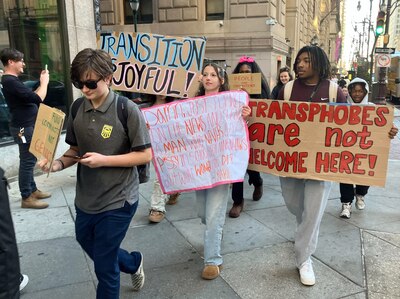 A group of students holding signs walk down the street.